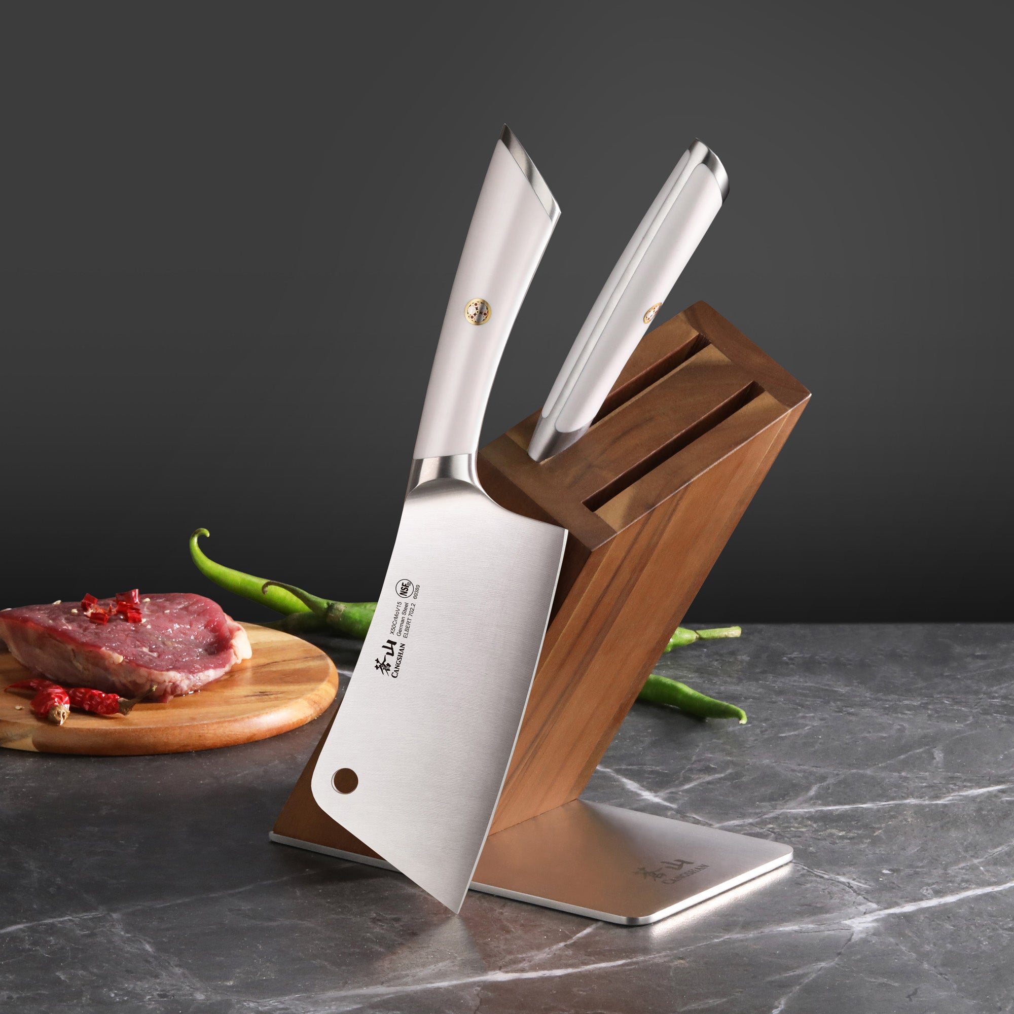 Two cleaver knives with white handles in a wooden block on a marble surface, with raw meat and green chili peppers nearby.