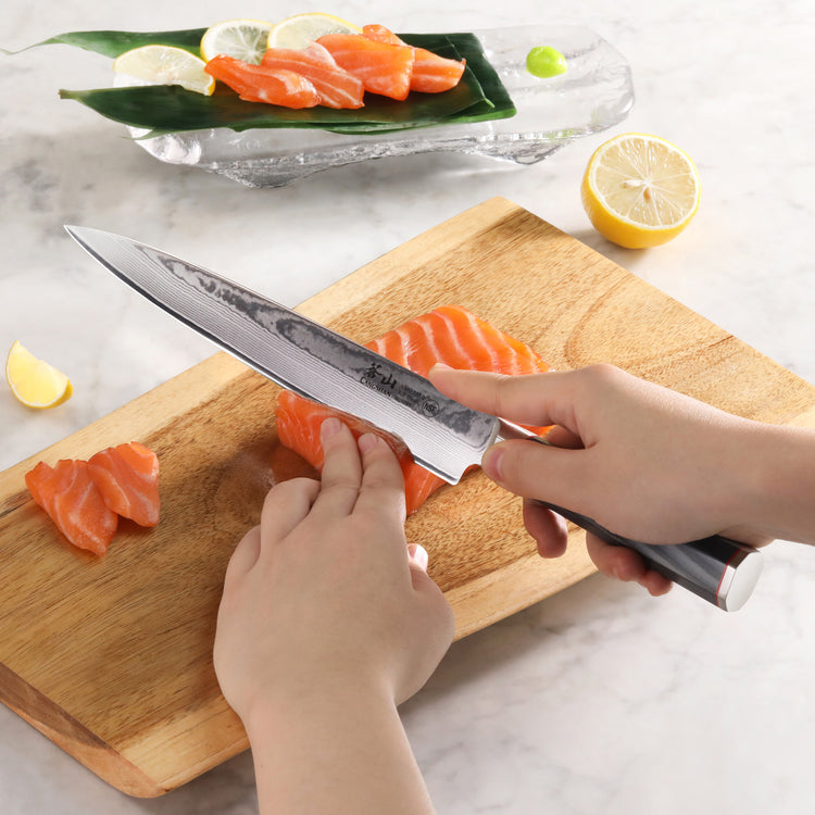Hands slicing raw salmon on a wooden board with an 8-inch Damascus steel sashimi knife.