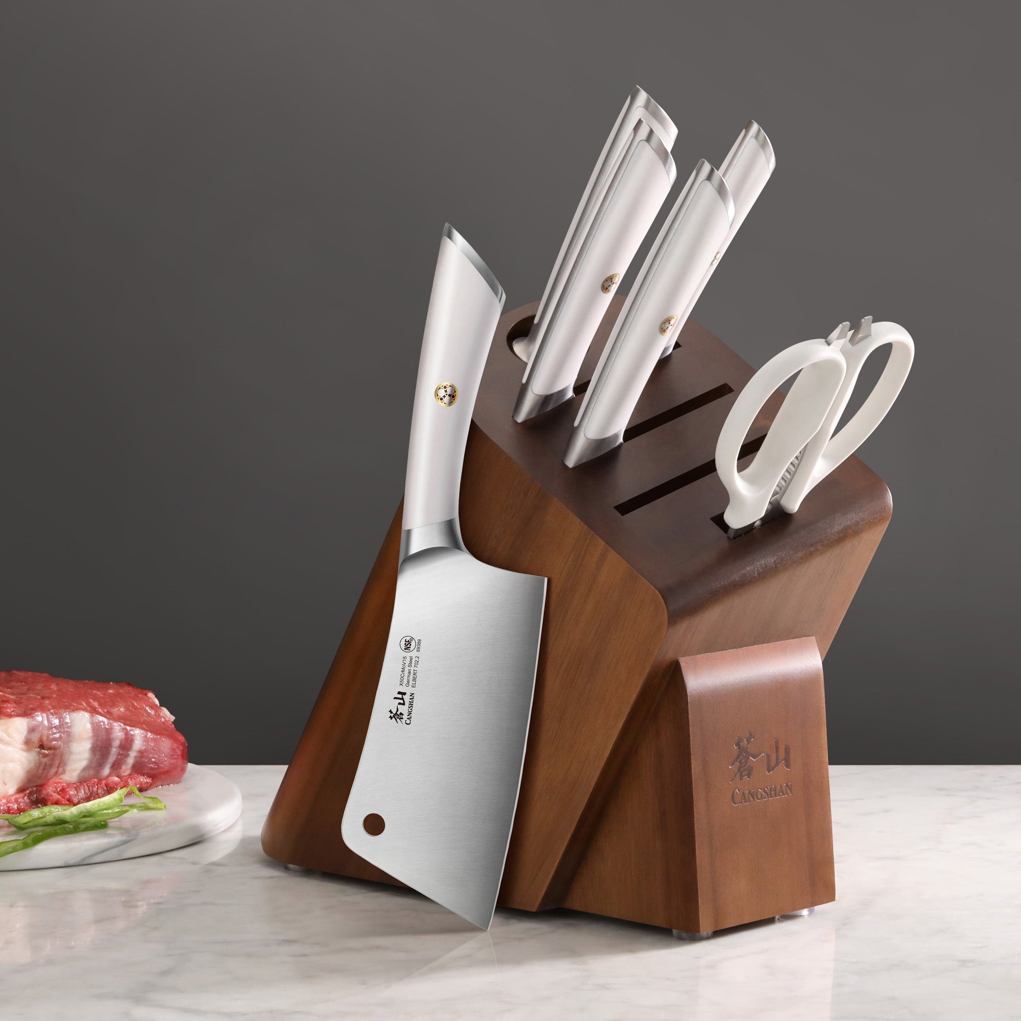 Wooden knife block holding four stainless steel knives and a pair of kitchen scissors on a marble surface.
