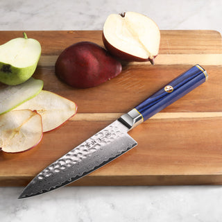 
                    
                      Chef knife with hammered Damascus steel blade and blue handle on wooden cutting board with sliced pears.
                    
                  