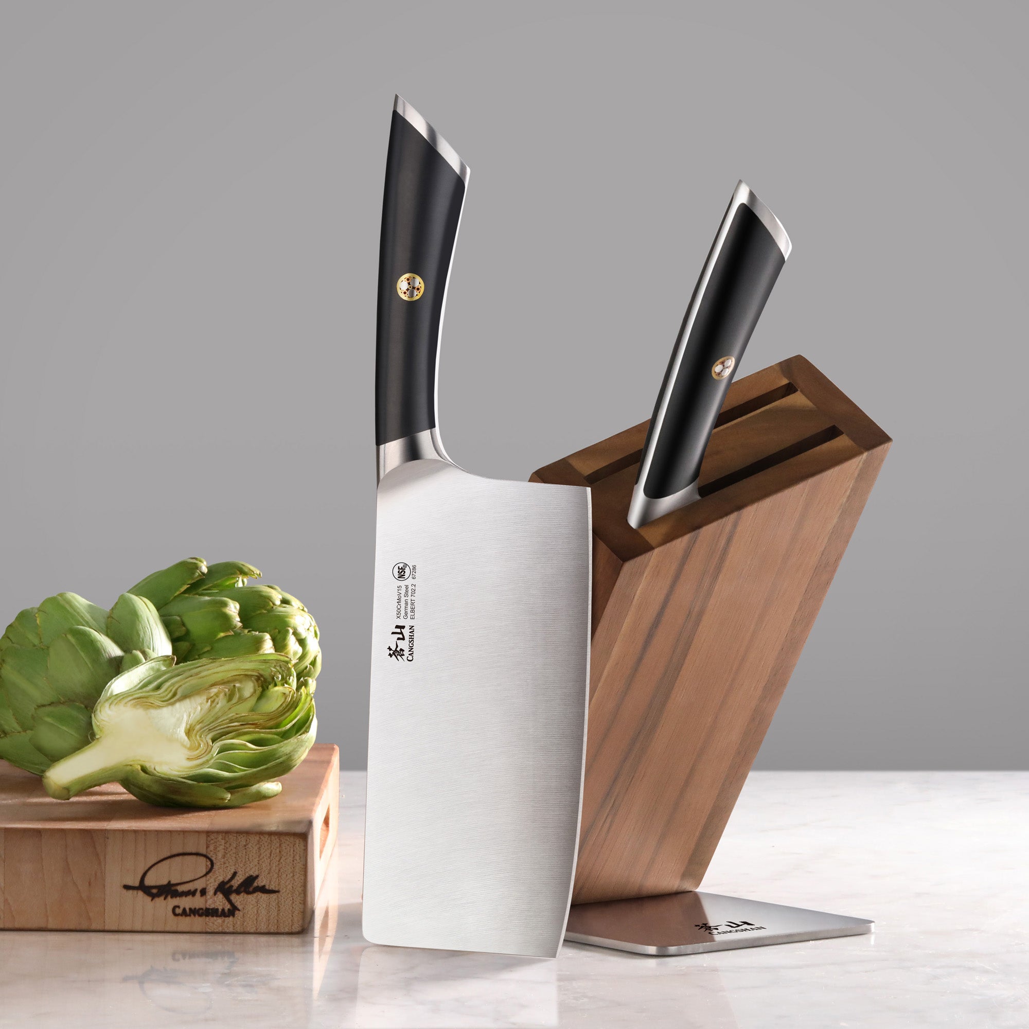 Two knives with black handles in and beside a wooden knife block on a marble surface, next to a halved artichoke.