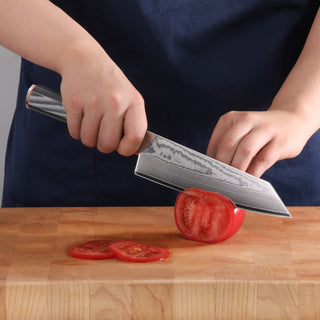 
                    
                      Person slicing a tomato on a wooden cutting board with a patterned blade Kiritsuke knife.
                    
                  
