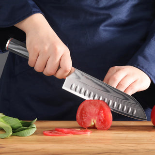 
                    
                      Hand holding YARI Series 7-Inch Santoku Knife slicing a tomato on a wooden cutting board.
                    
                  