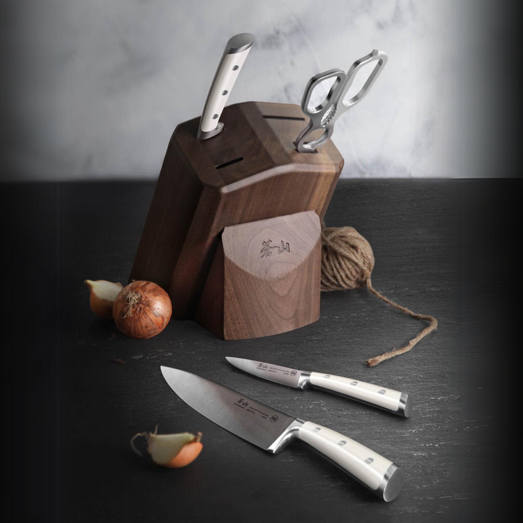 Wooden knife block with two knives and scissors, two onions, and a ball of twine on a dark surface.