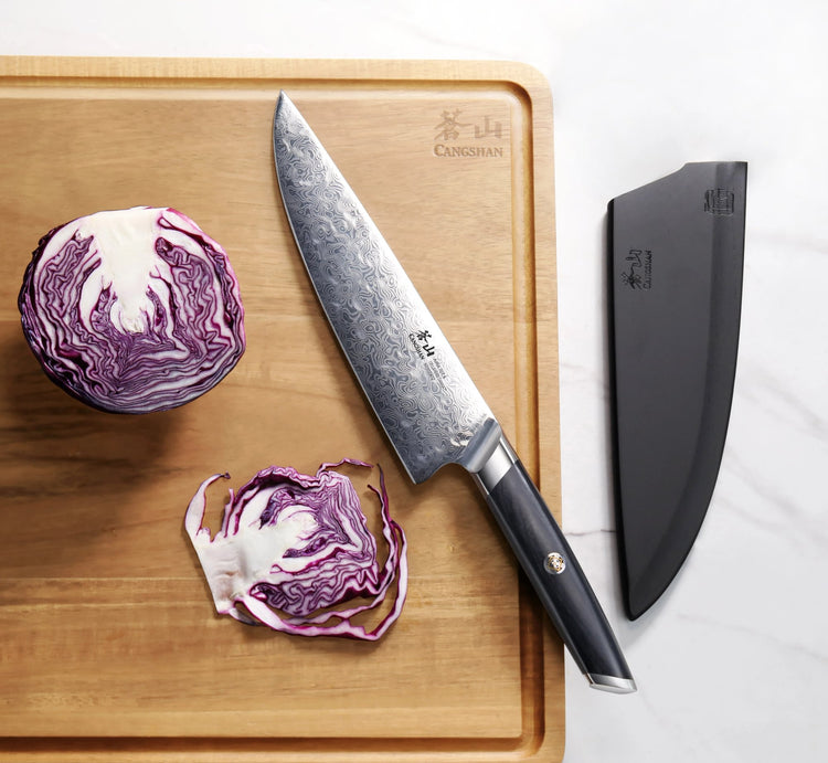 AIRA Series 8-Inch Chef’s Knife with Damax steel on a cutting board next to a red cabbage and black sheath.
