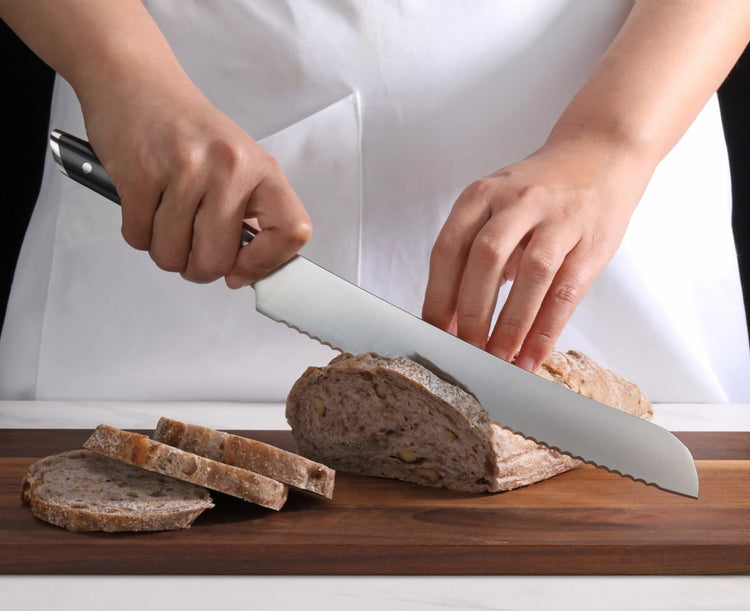 Person slicing a loaf of bread on a wooden cutting board using a serrated knife with a black handle.