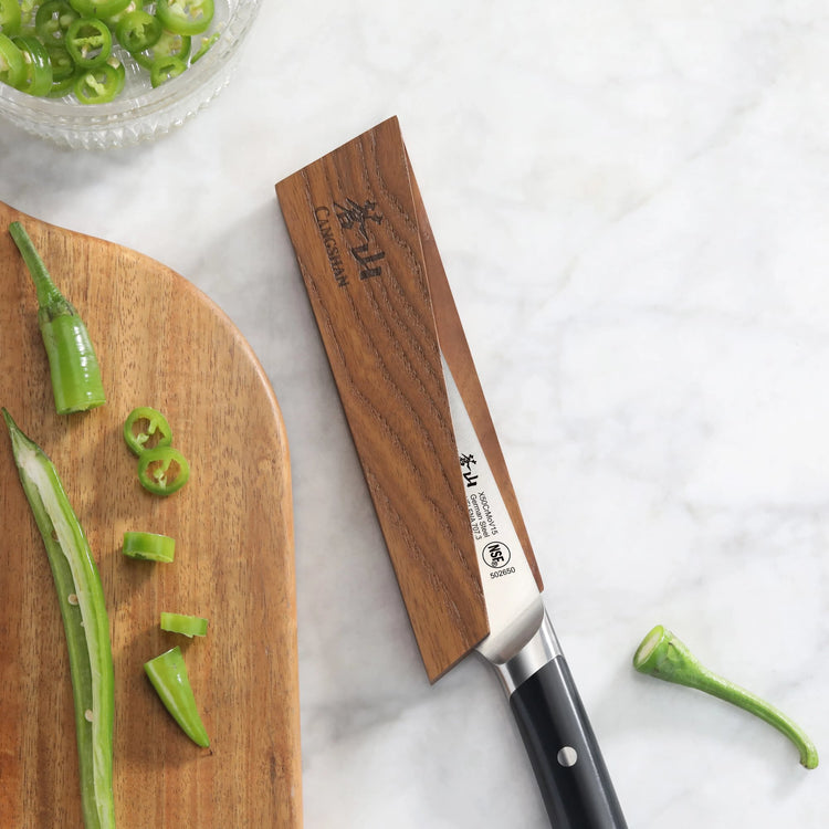 Ash wood magnetic knife sheath covering the blade of a kitchen knife with a black handle on a marble surface.
