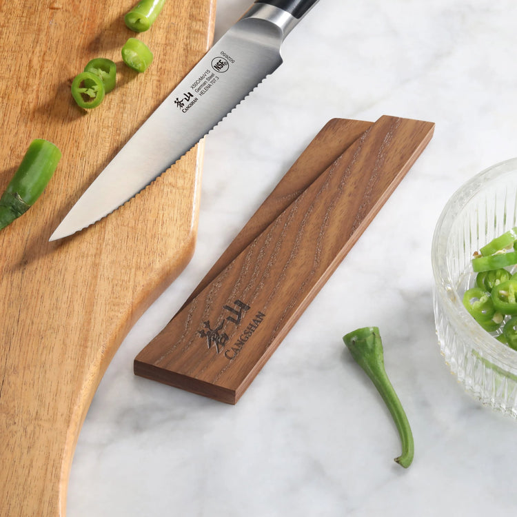 Ash wood magnetic knife sheath holding a serrated knife next to sliced green peppers on a wooden cutting board.