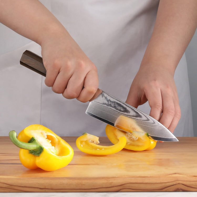 Chef slicing a yellow bell pepper with a MAYA Series 6-inch Damascus steel chef’s knife on a wooden board.