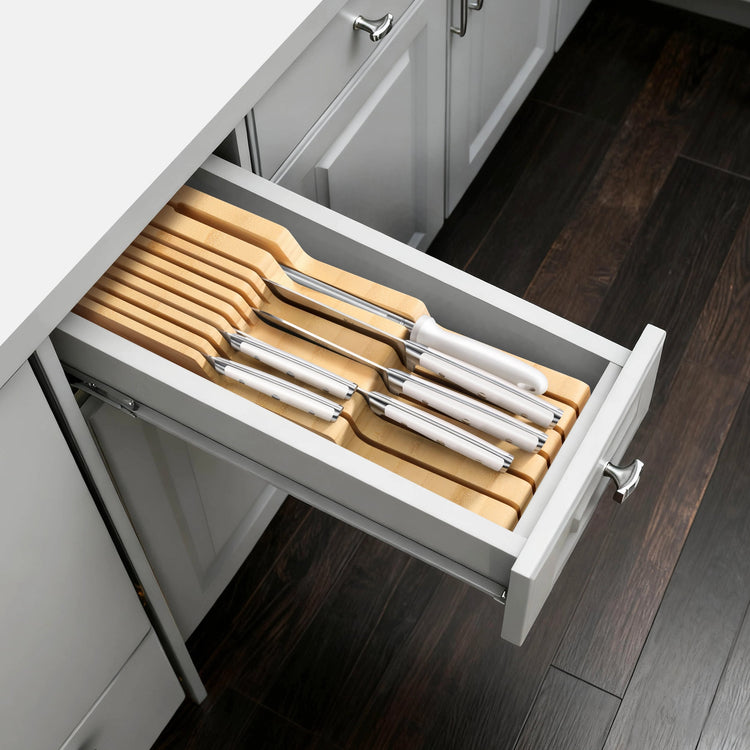 Seven knives with stainless steel blades and light wooden handles neatly arranged in an open kitchen drawer.