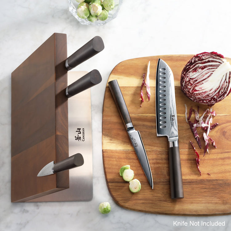 Magnetic wooden knife block holding three knives next to a cutting board with two knives and chopped vegetables.