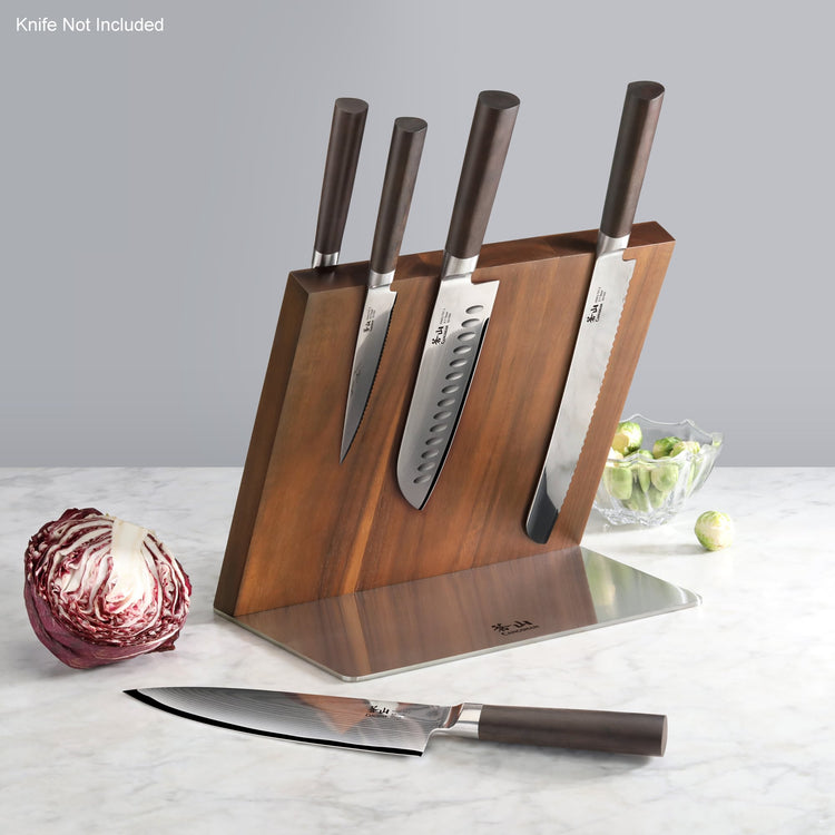 Wooden magnetic knife block holding four knives with dark handles, placed on a marble countertop next to a cabbage and a bowl