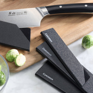 
                    
                      Set of six black knife edge guards with textured surfaces on a wooden cutting board next to a kitchen knife and Brussels spro
                    
                  