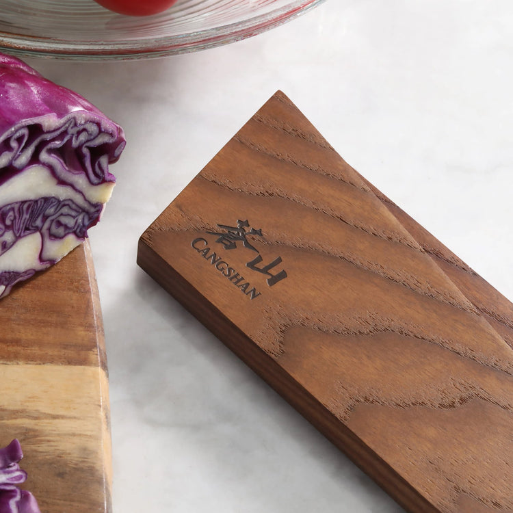 Rectangular ash wood magnetic knife sheath with engraved logo, placed on a marble surface near sliced purple cabbage.