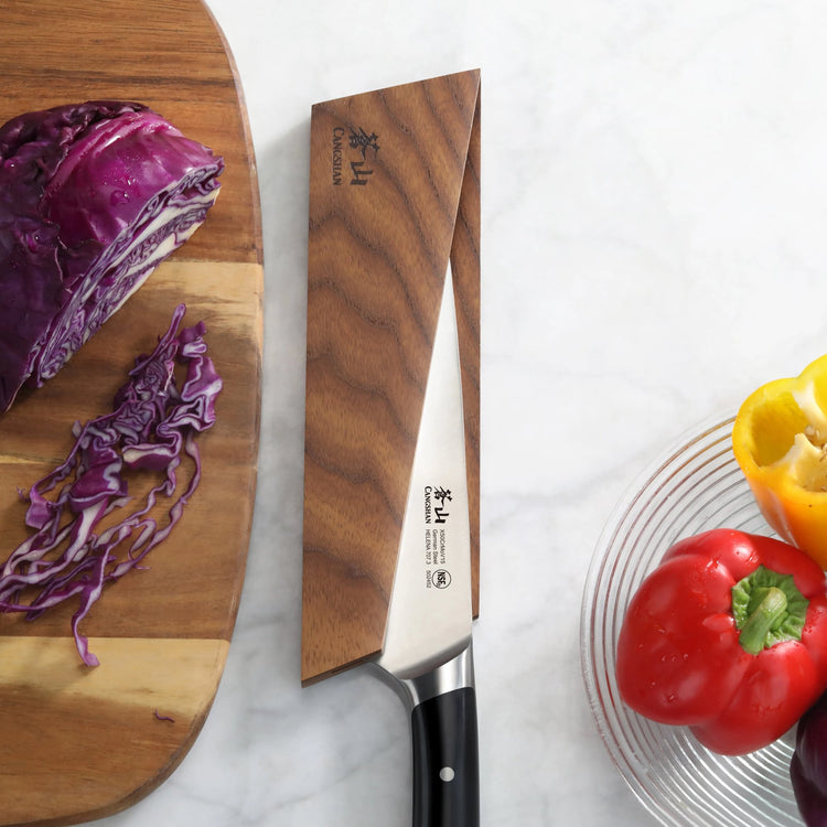 Ash wood magnetic knife sheath covering the blade of a kitchen knife on a marble countertop.