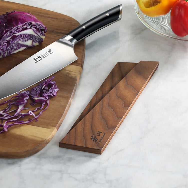 Ash wood magnetic knife sheath next to a chef's knife slicing purple cabbage on a wooden cutting board.