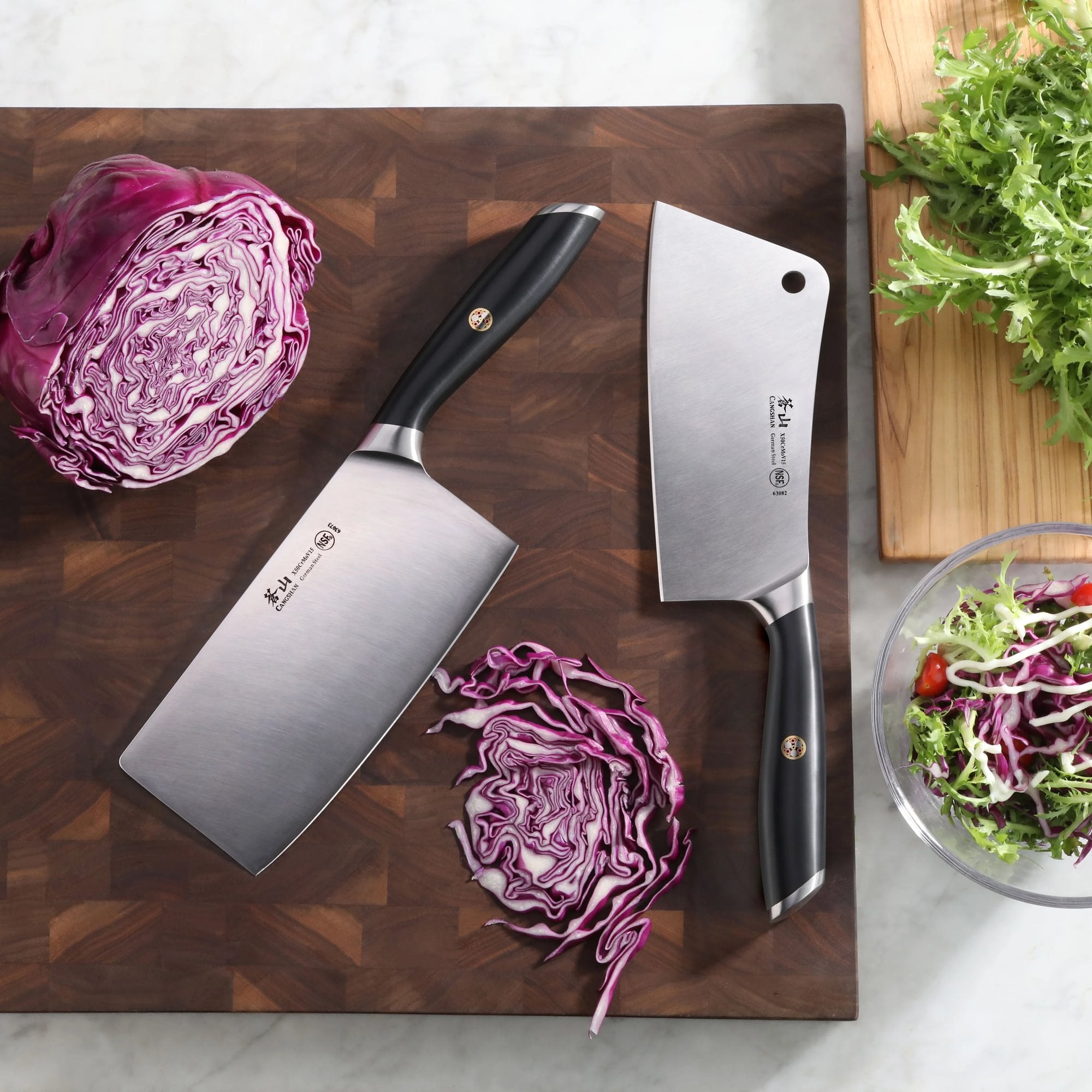 Two cleavers with black handles on a wooden cutting board, surrounded by sliced red cabbage and a bowl of salad.