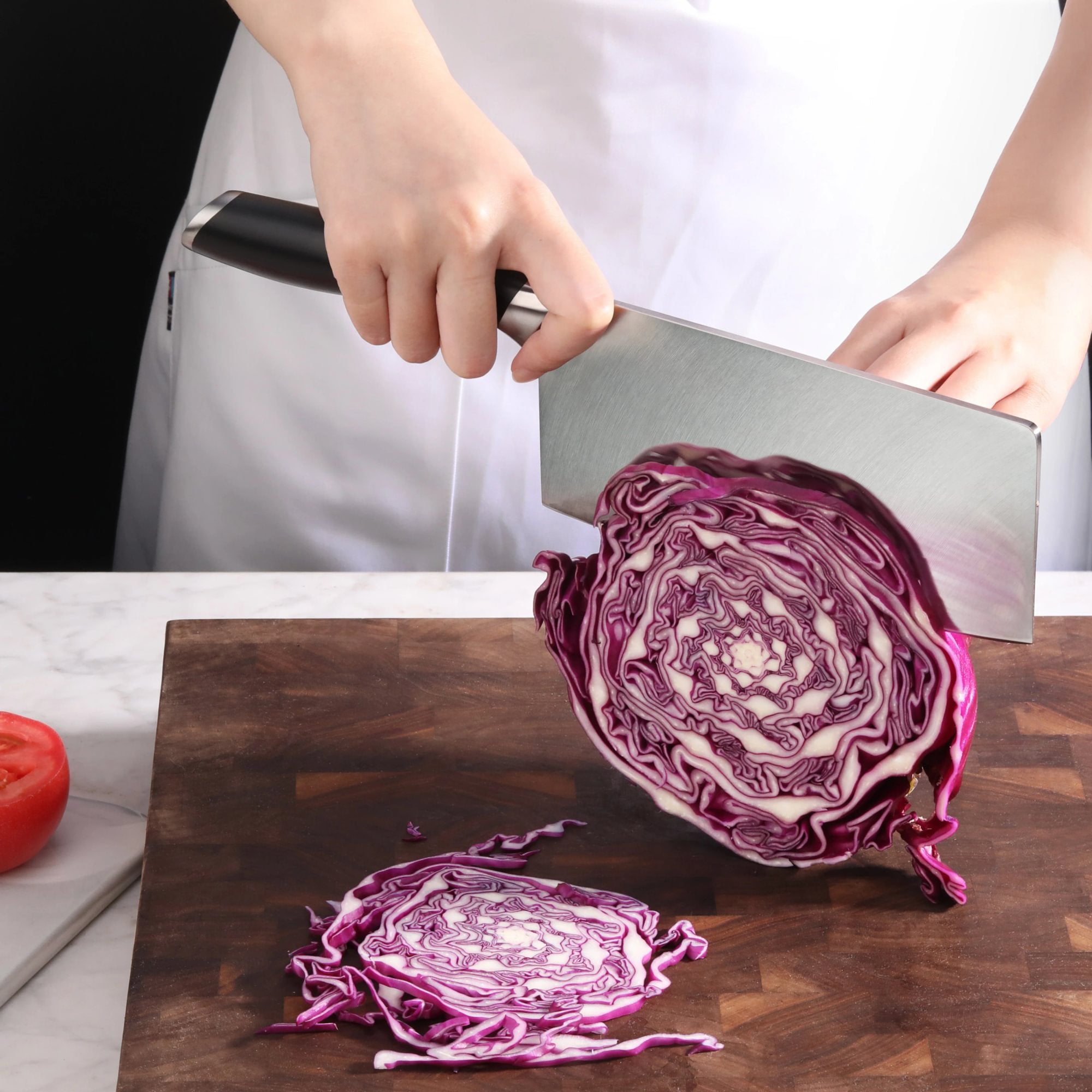 Hand holding a cleaver slicing a halved purple cabbage on a wooden cutting board.