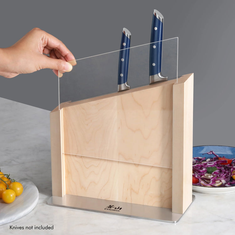Hand lifting clear blade guard on maple magnetic knife block holding two knives with blue handles.