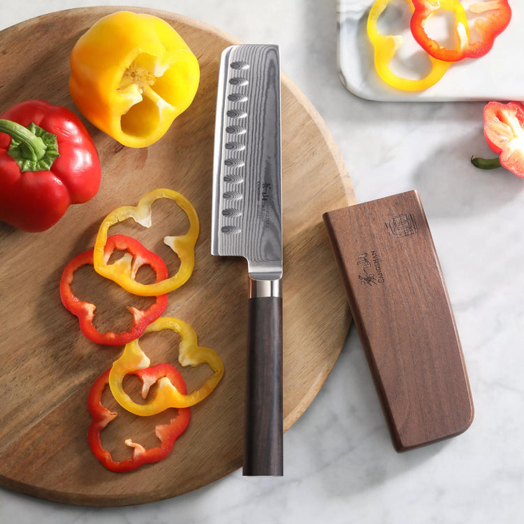 Nakiri knife with wooden handle and sheath on a cutting board with sliced red and yellow bell peppers.