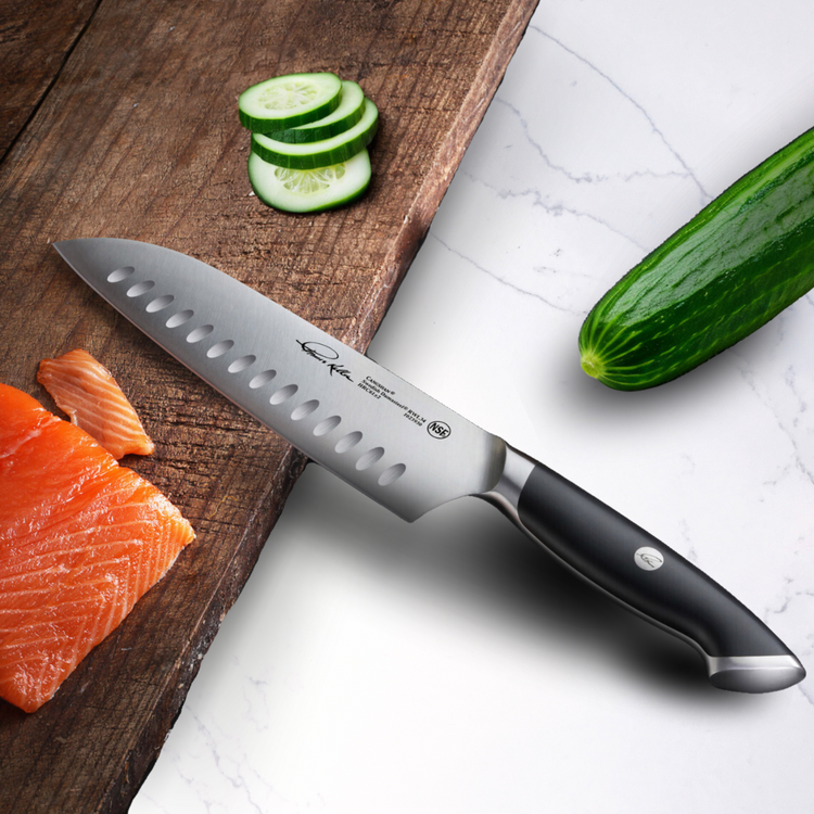 TKSC 7-inch Santoku knife with black handle slicing cucumber on wooden cutting board next to salmon fillet and whole cucumber