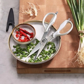 
                    
                      White-handled kitchen shears with blade holder beside chopped green onions and red chili peppers on a plate.
                    
                  