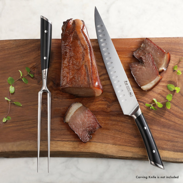6-inch carving fork with black handle and two prongs on wooden cutting board with sliced roast beef and carving knife.