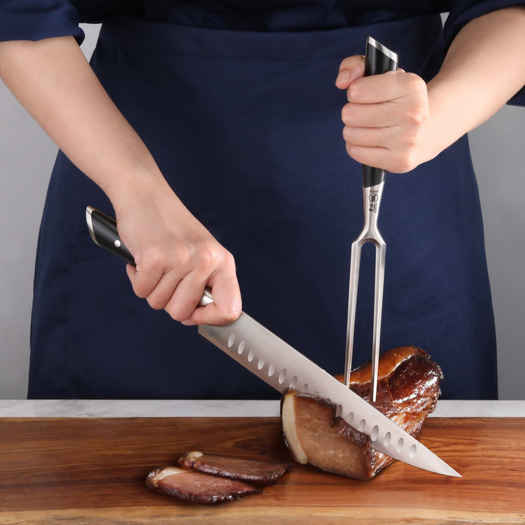 Person using a carving fork and knife to slice cooked meat on a wooden cutting board.