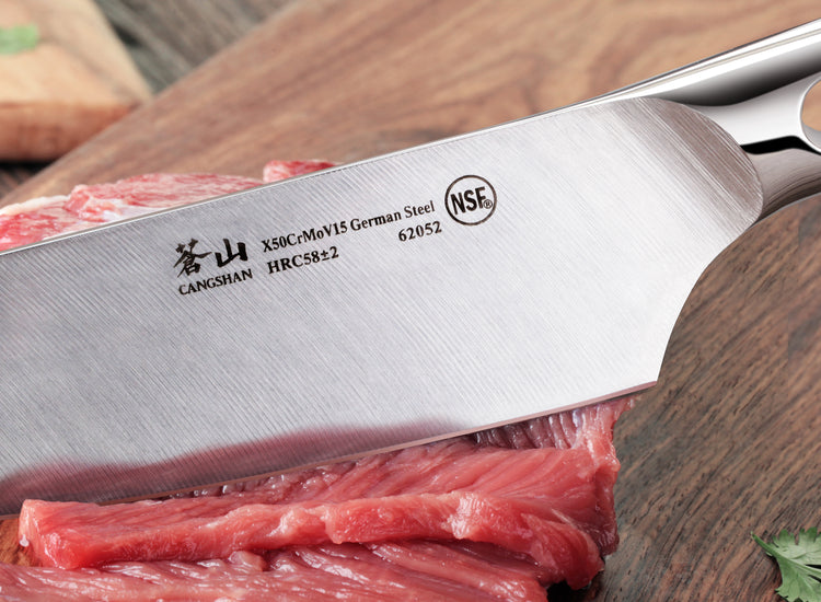 Close-up of a forged German steel knife blade cutting raw meat on a wooden surface.