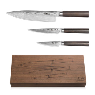 
                    
                      Three Damascus steel knives with dark wooden handles displayed above a matching walnut storage box with knife outlines.
                    
                  