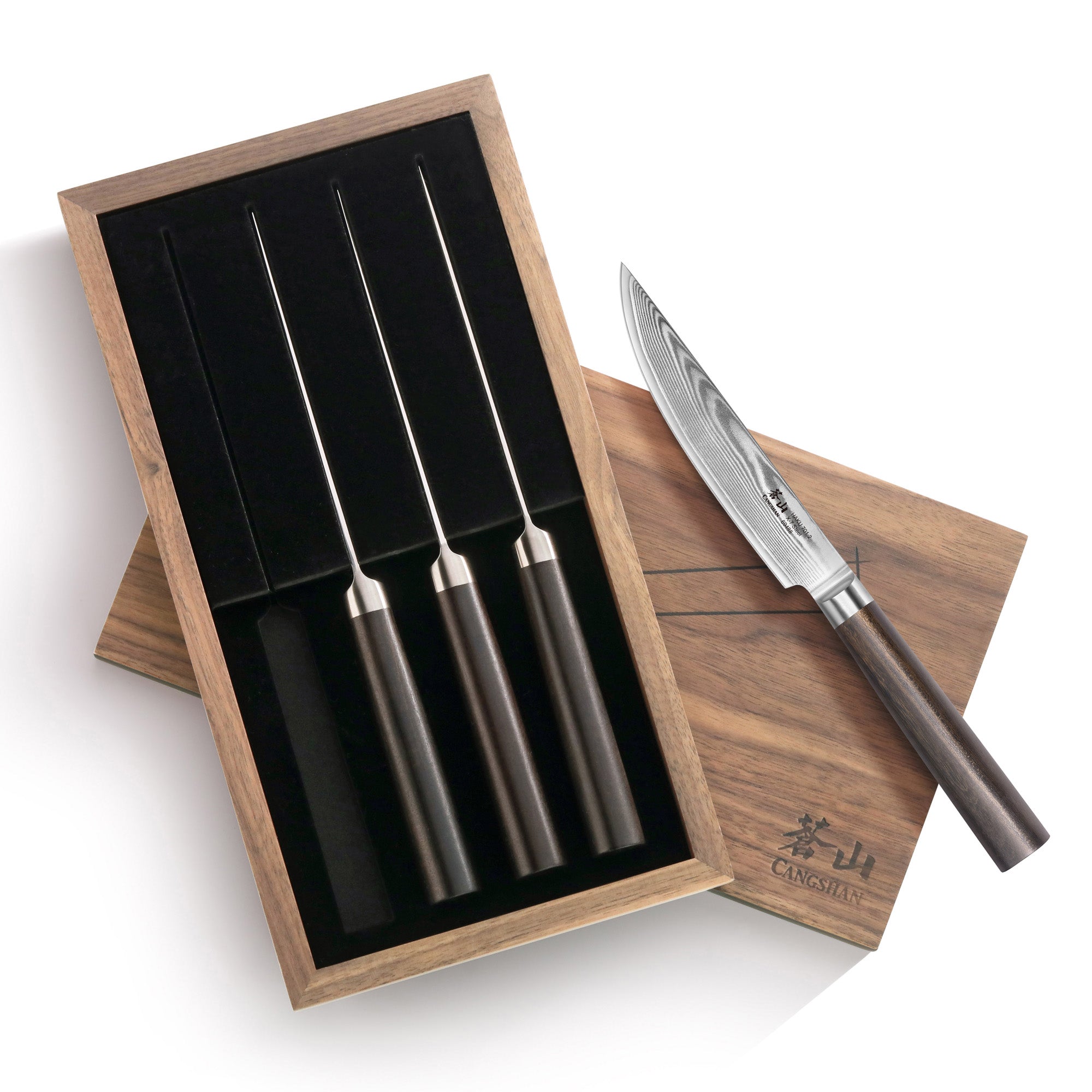 Four steak knives with dark handles in a wooden box, one knife resting on the box lid showing a patterned steel blade.