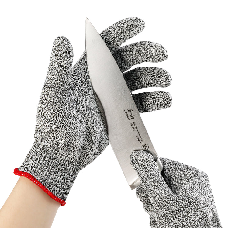 Hands wearing gray cut resistant gloves holding a large kitchen knife with a silver blade.