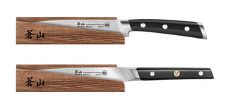 
                    
                      Two kitchen knives with black handles resting on solid ash wood magnetic sheaths with Japanese characters.
                    
                  
