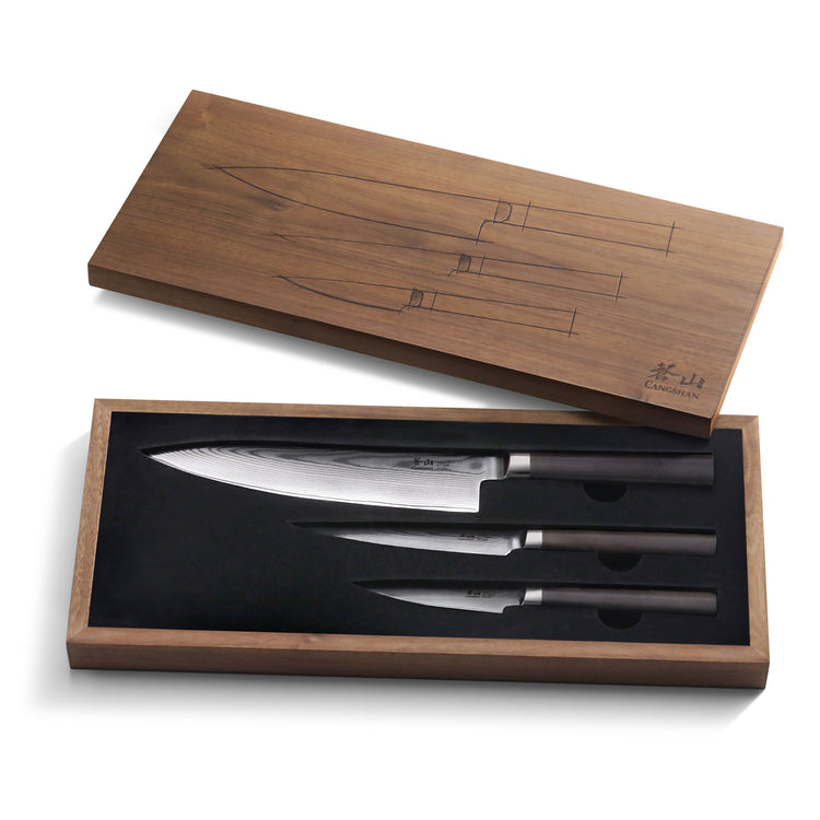 Three Damascus steel knives with black handles in a walnut box with a matching lid featuring knife outlines.