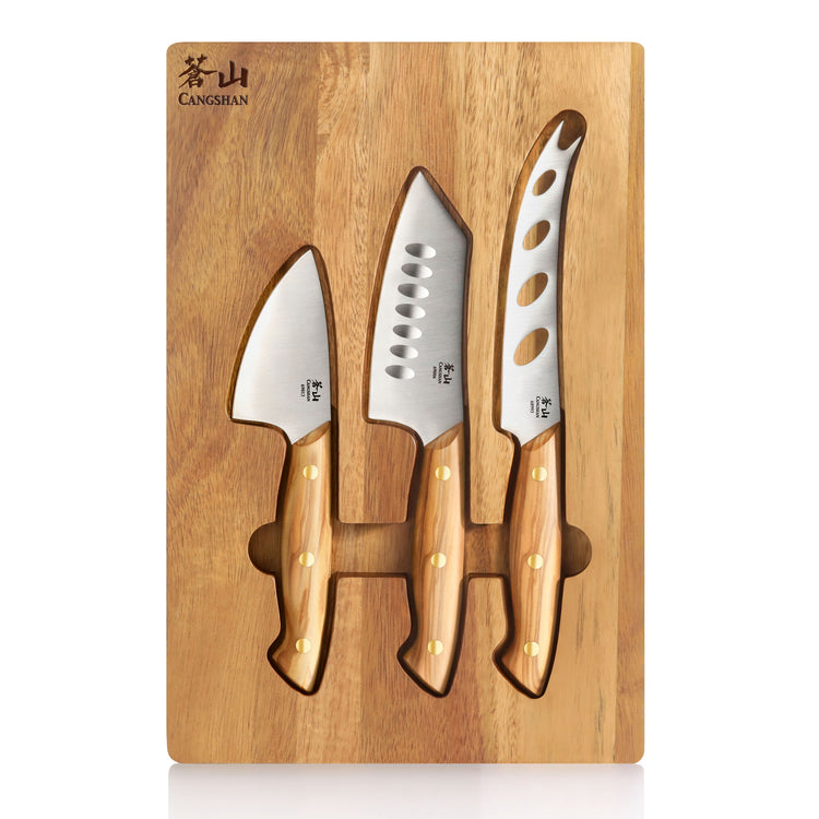 Three cheese knives with olive wood handles on an acacia wood board with cutouts for each knife.