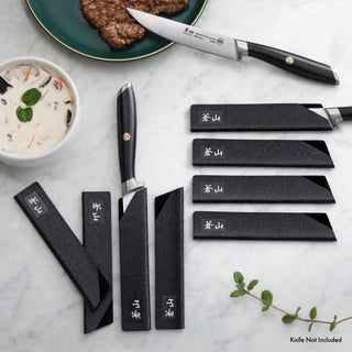 
                    
                      Eight black textured knife guards of varying sizes arranged on a marble surface, with one guard partially covering a steak kn
                    
                  