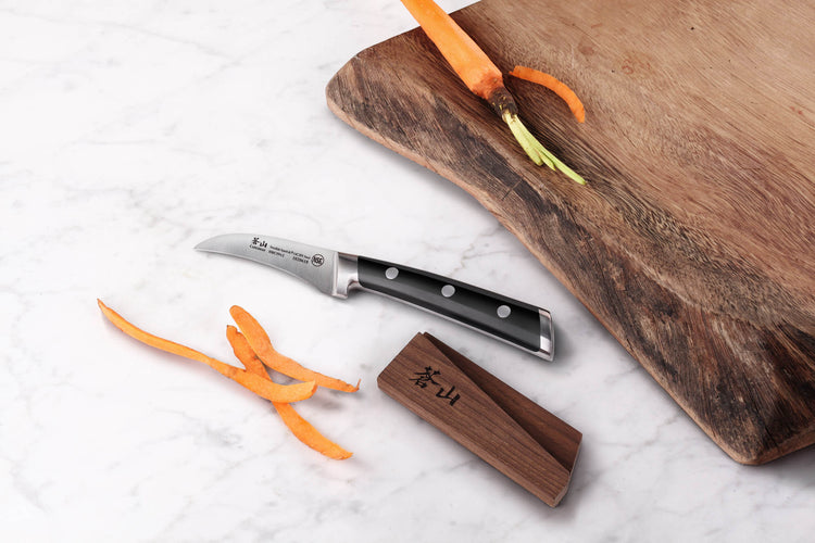 2.75-inch peeling knife with black handle and ash wood sheath next to peeled carrot and wooden cutting board.