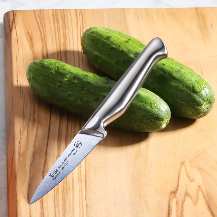 Stainless steel knife with ergonomic handle resting on two whole cucumbers on a wooden cutting board.