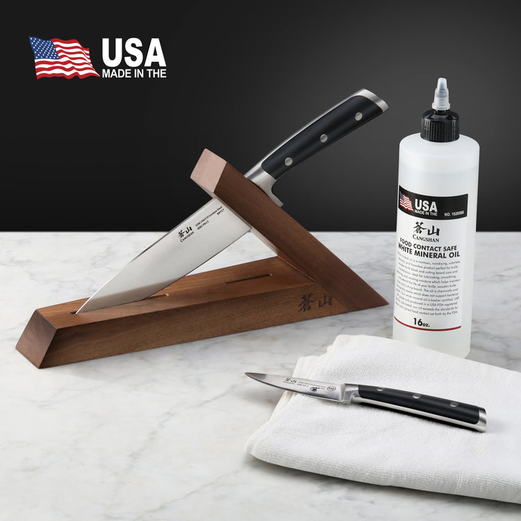 Bottle of white mineral oil for blade protection next to a knife in a wooden stand and a folding knife on a white cloth.