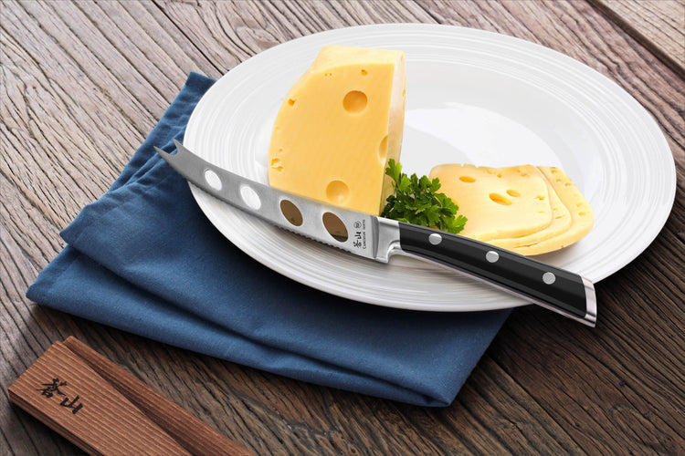 Cheese knife with holes on white plate next to sliced Swiss cheese and parsley on blue napkin.