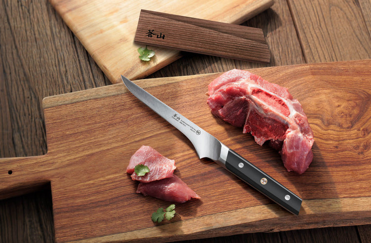 Raw pork chop with bone and two slices on a wooden cutting board next to a kitchen knife.