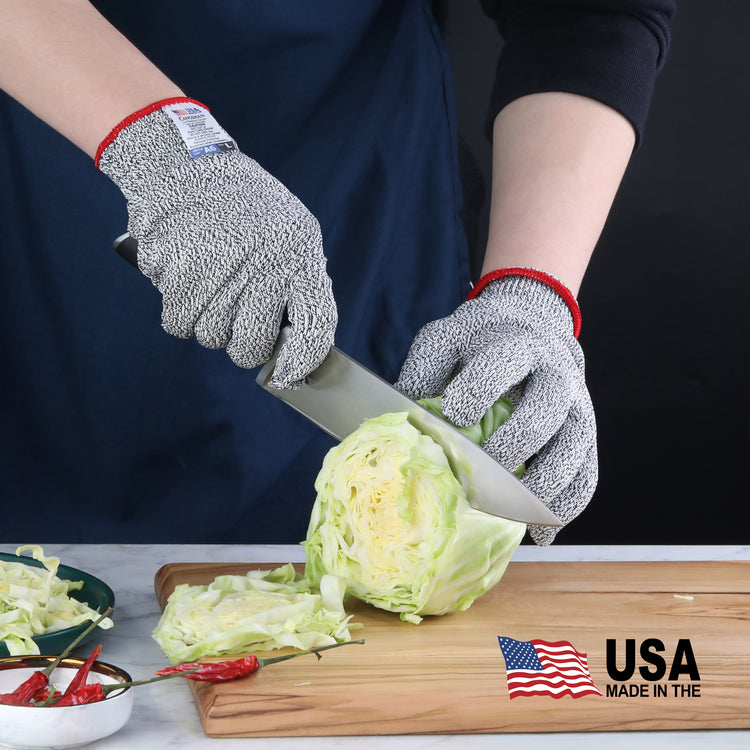 Hands wearing gray cut resistant gloves slicing a head of cabbage on a wooden cutting board.