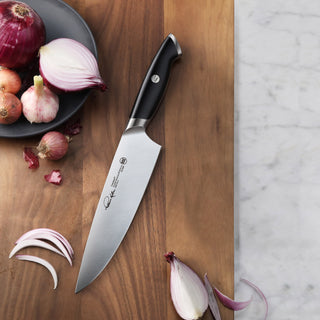 
                    
                      8-inch chef's knife with black handle on wooden cutting board next to sliced and whole onions and garlic cloves.
                    
                  