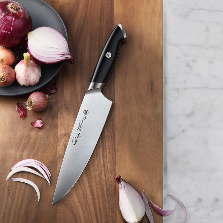 8-inch chef's knife with black handle on wooden cutting board next to sliced and whole onions and garlic cloves.