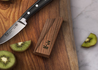
                    
                      Solid ash wood magnetic knife sheath placed on a wooden cutting board next to a paring knife and sliced kiwi.
                    
                  