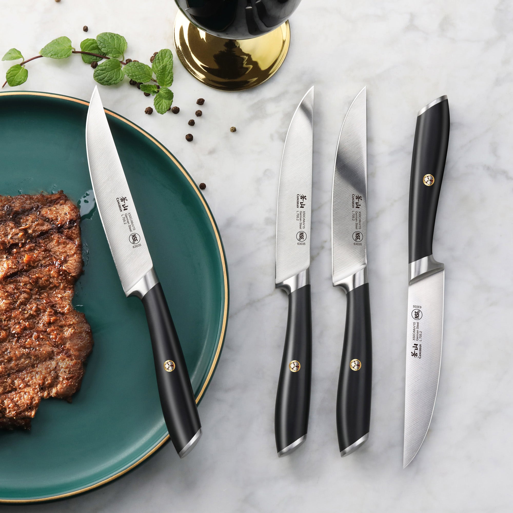 Four steak knives with black handles and forged German steel blades, one cutting a cooked steak on a green plate.