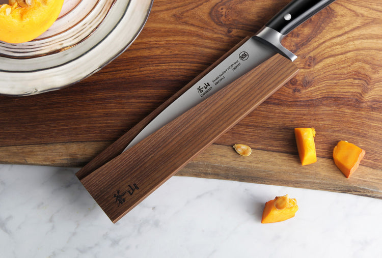 Magnetic knife sheath made of solid ash wood holding a kitchen knife on a wooden cutting board with pumpkin pieces nearby.