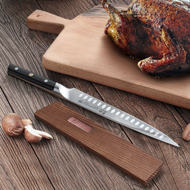 Long, narrow kitchen knife with black handle resting next to a solid ash wood magnetic knife sheath on a wooden surface.