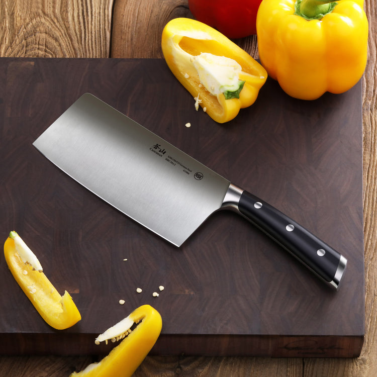 Cleaver knife with black handle on wooden cutting board next to sliced yellow bell peppers.