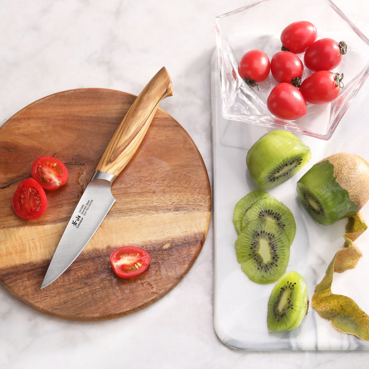 Paring knife with olivewood handle on wooden board next to halved cherry tomatoes and sliced kiwi with peel on marble surface
